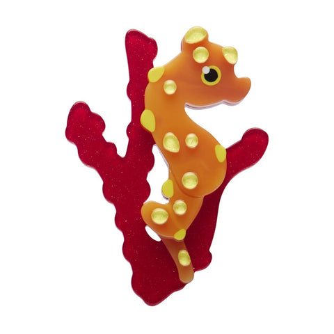An Erstwilder Pygmy Seahorse resin brooch featuring an orange and yellow seahorse, attached to a red coral.