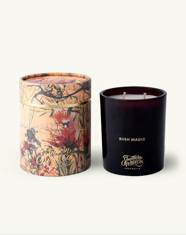 A soy wax candle with a dark glass container, next to a cylindrical paper tube with floral design.