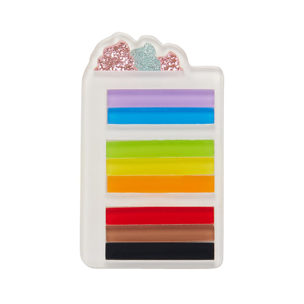 A brooch resembling a slice of cake with colorful Pride Flag layers and topped with glitter, designed by Erstwilder.