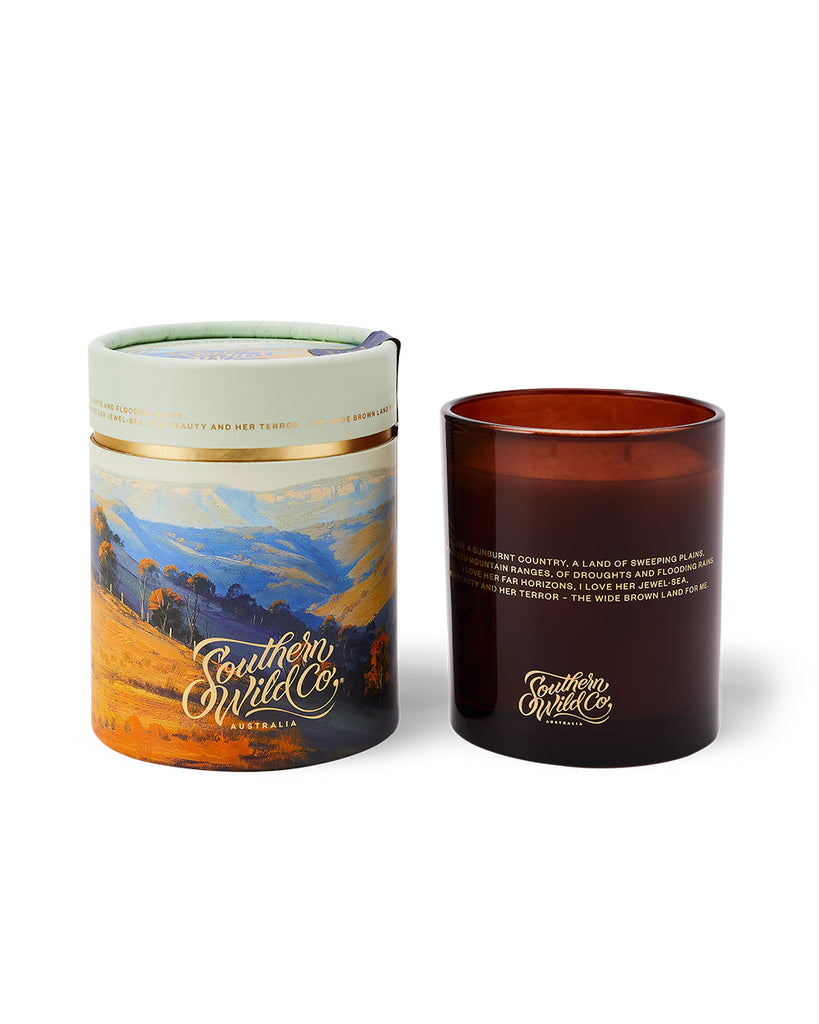 A 300g candle with an artistic representation of a bush landscape, alongside its recyclable kraft paper packaging.