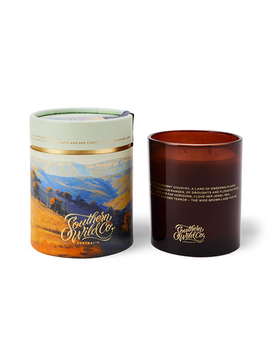 A 300g candle with an artistic representation of a bush landscape, alongside its recyclable kraft paper packaging.