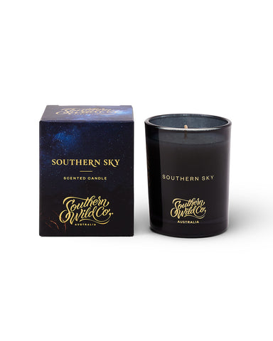 A dark blue glass candle next to its packaging box, both featuring gold and white text against a background with a starry night sky motif.
