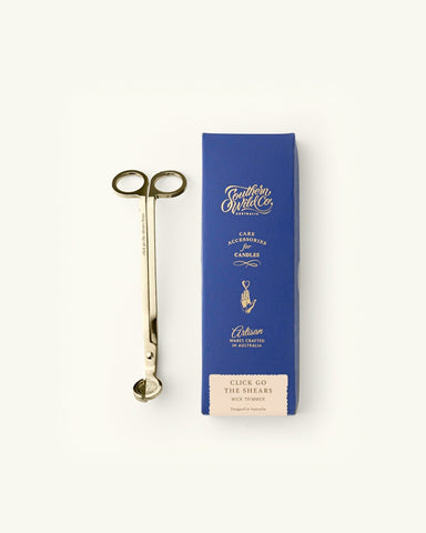 A pair of gold-plated wick trimmers next to its packaging box with 'Southern Wild Co' branding.