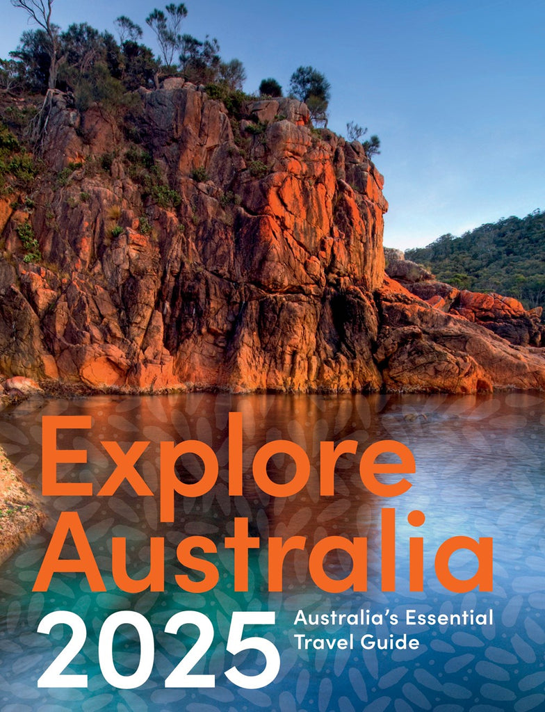 Cover of 'Explore Australia 2025' travel guide featuring a vibrant landscape with red rocks and a body of water in the foreground, with the title and year prominently displayed.