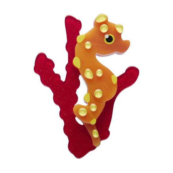 An Erstwilder Pygmy Seahorse resin brooch featuring an orange and yellow seahorse, attached to a red coral.