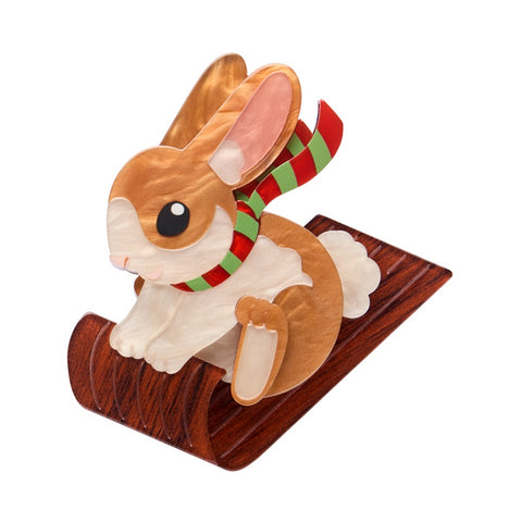 Erstwilder Breezy the Bunny layered brooch features a brown rabbit wearing a green a red scarf on a wooden toboggan.