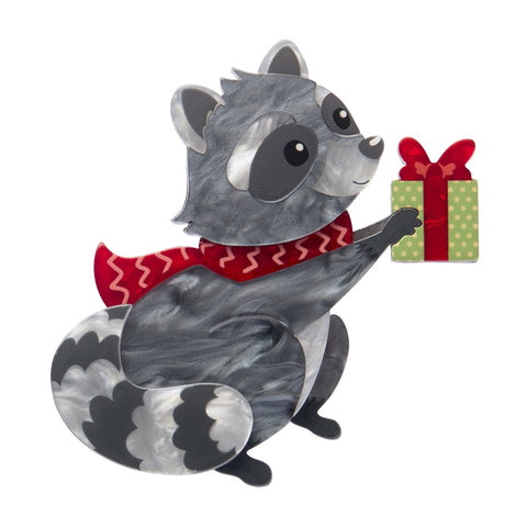 Erstwilder Rhi-Rhi the Raccoon brooch in grey layered resin, bearing a gift and wearing a red scarf.