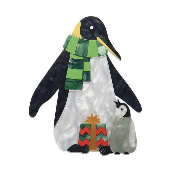 Erstwilder Paddy & Pip the Penguins layered resin brooch shows an adult penguin with a green striped scarf and a gift in their feet, with a baby penguin at its side.