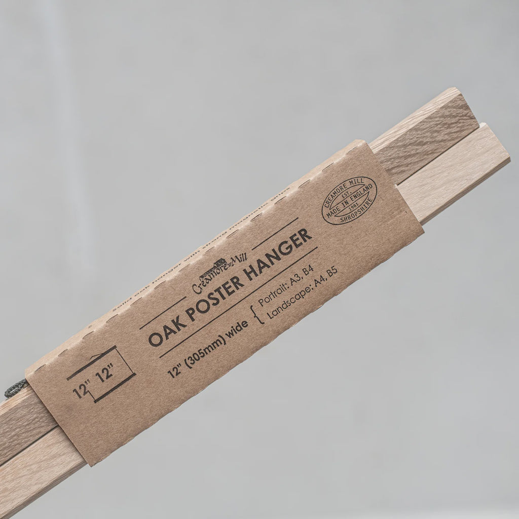 An oak poster hanger with strong magnetic grips, natural oak bars, and a fixed cord, packaged in a cardboard sleeve with branding and product information.