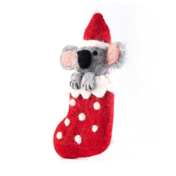 A felt koala ornament wearing a red Santa hat and sitting in a red stocking with white polka dots, hanging from a red and white string on a white background.