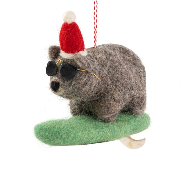 Decorative wombat ornament with a Santa hat, sunglasses riding a green surfboard hanging from a red-and-white string on a white background