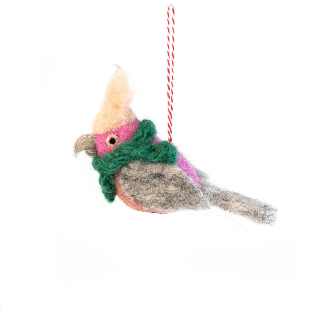 A felted bird ornament wearing a green scarf, hanging from a red and white striped string against a white background.