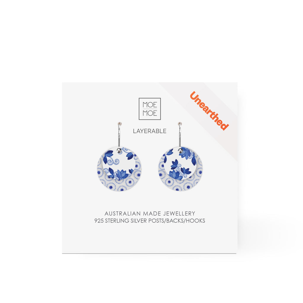 A pair of earrings featuring a blue and white pattern on two round discs of different sizes.