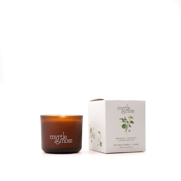 A brown glass soy wax candle with a label that reads 'Myrtle & Moss', alongside its white packaging box with the same brand and product details.