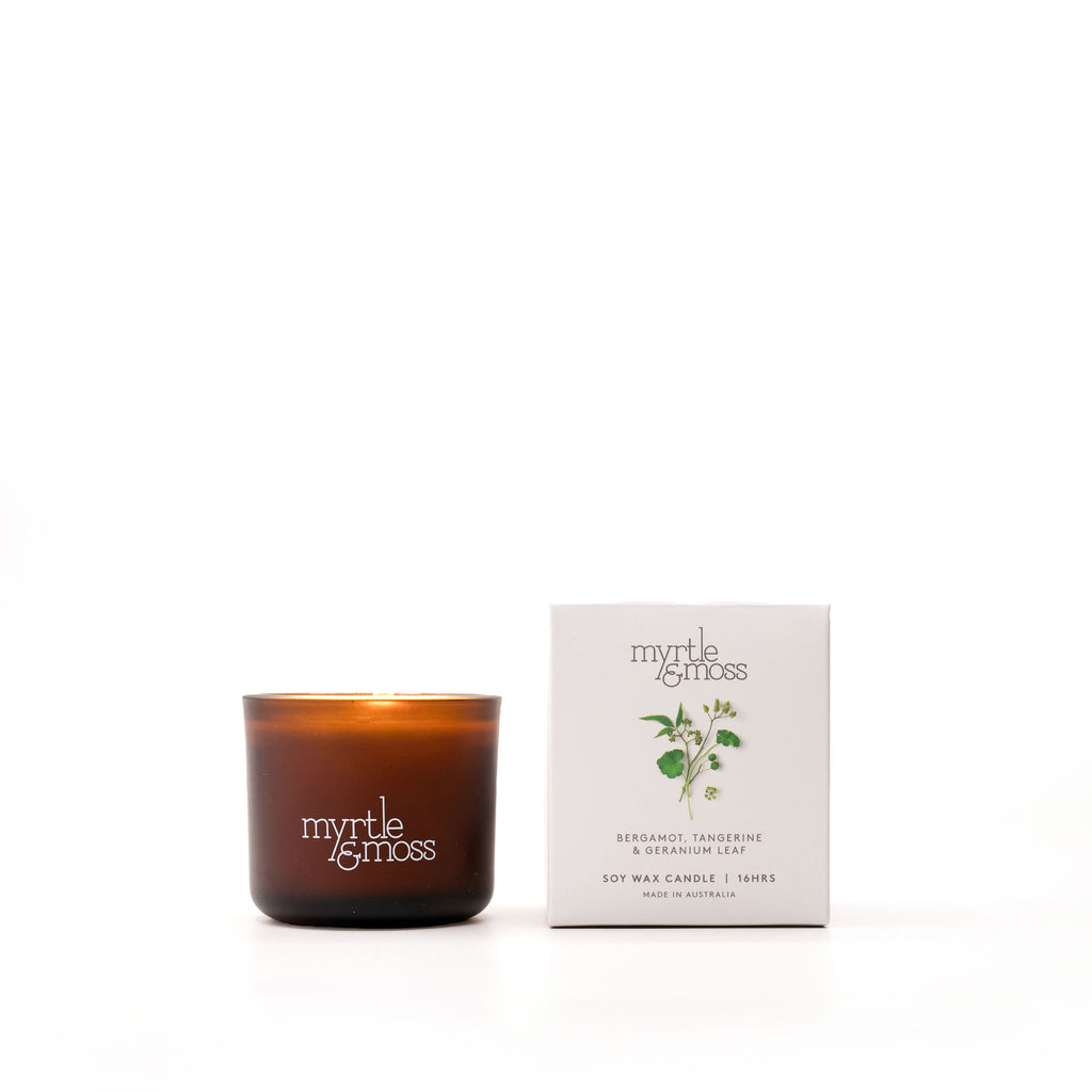 A brown glass soy wax candle with a label that reads 'Myrtle & Moss', alongside its white packaging box with the same brand and product details.