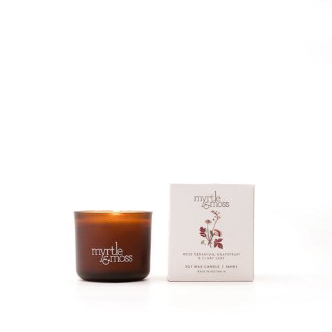 A brown glass soy wax candle with a label that reads 'Myrtle & Moss', alongside its white packaging box with the same brand and product details.