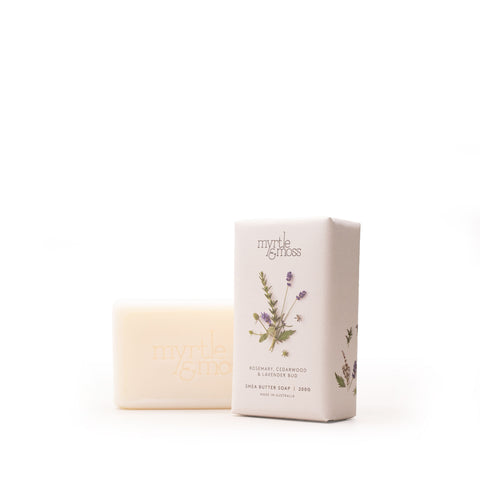 A bar of Myrtle & Moss shea butter soap in a pale cream color stands next to its matching rectangular packaging box on a seamless white background. The box features a botanical illustration of lavender and rosemary with the brand name 'myrtle & moss' printed at the top.