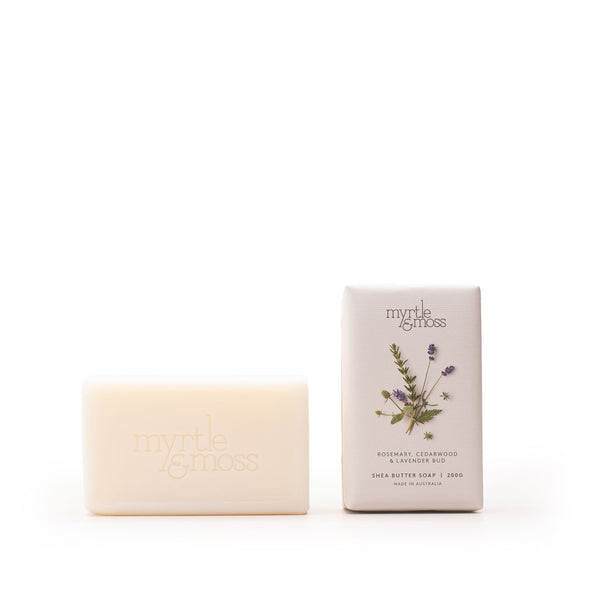 A bar of Myrtle & Moss shea butter soap in a pale cream color stands next to its matching rectangular packaging box on a seamless white background. The box features a botanical illustration of lavender and rosemary with the brand name 'myrtle & moss' printed at the top.