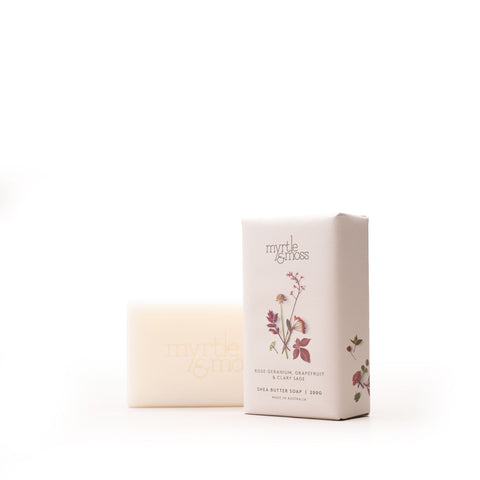 A bar of Myrtle & Moss unscented grapefruit and clary sage milk butter soap stands next to its paper packaging box on a seamless white background.