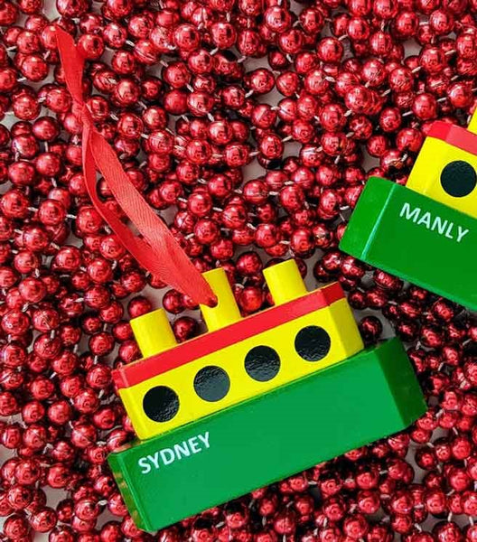 Colorful wooden ferry ornament with 'Sydney' and 'Manly' labels on a red beaded gzrland background