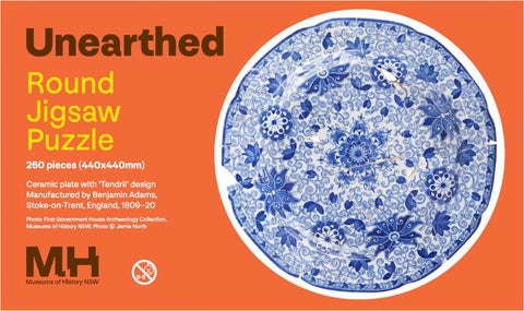 Unearthed round jigsaw puzzle packaging with blue and white floral design on an orange background