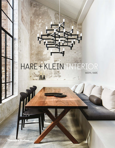 Cover of the book 'Hare + Klein Interior' featuring a modern interior design of a dining space with a large wooden table, black chairs, and a contemporary chandelier with exposed concrete walls.