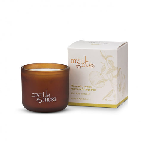 A brown glass soy wax candle with a label that reads 'Myrtle & Moss', alongside its white packaging box with the same brand and product details.