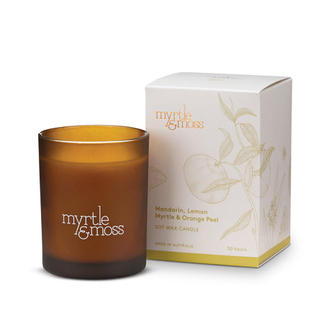 A brown glass soy wax candle with a label that reads 'Myrtle & Moss'. The candle is displayed in front of its white packaging box with leaf patterns.