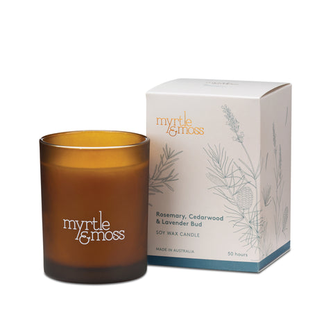 A lavender soy wax candle by Myrtle & Moss in an amber glass jar, next to its packaging box featuring botanical designs.