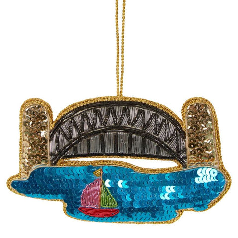 A sequin decoration featuring a Sydney harbour scene with a bridge, sailboat, and water, accented with gold trim and beading.